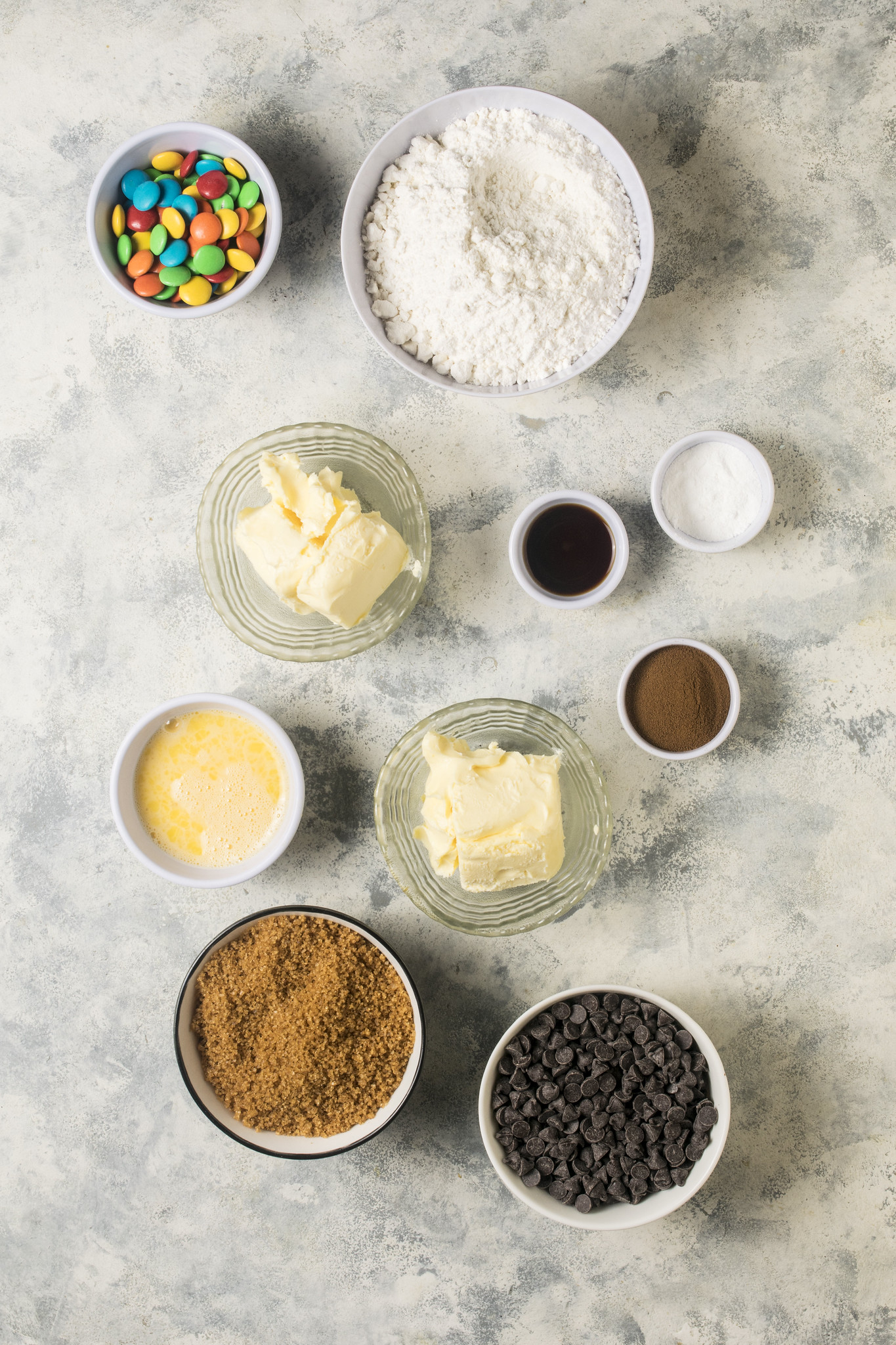 Measured ingredients for browned butter chocolate chip cookies, including butter, flour, brown sugar, beaten egg, chocolate chips and M&Ms.